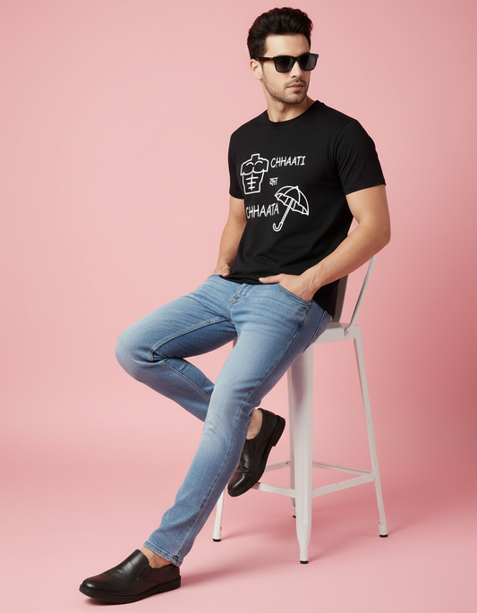 Man wearing a black t-shirt with white graphics and text, sitting on a white stool against a pink background.