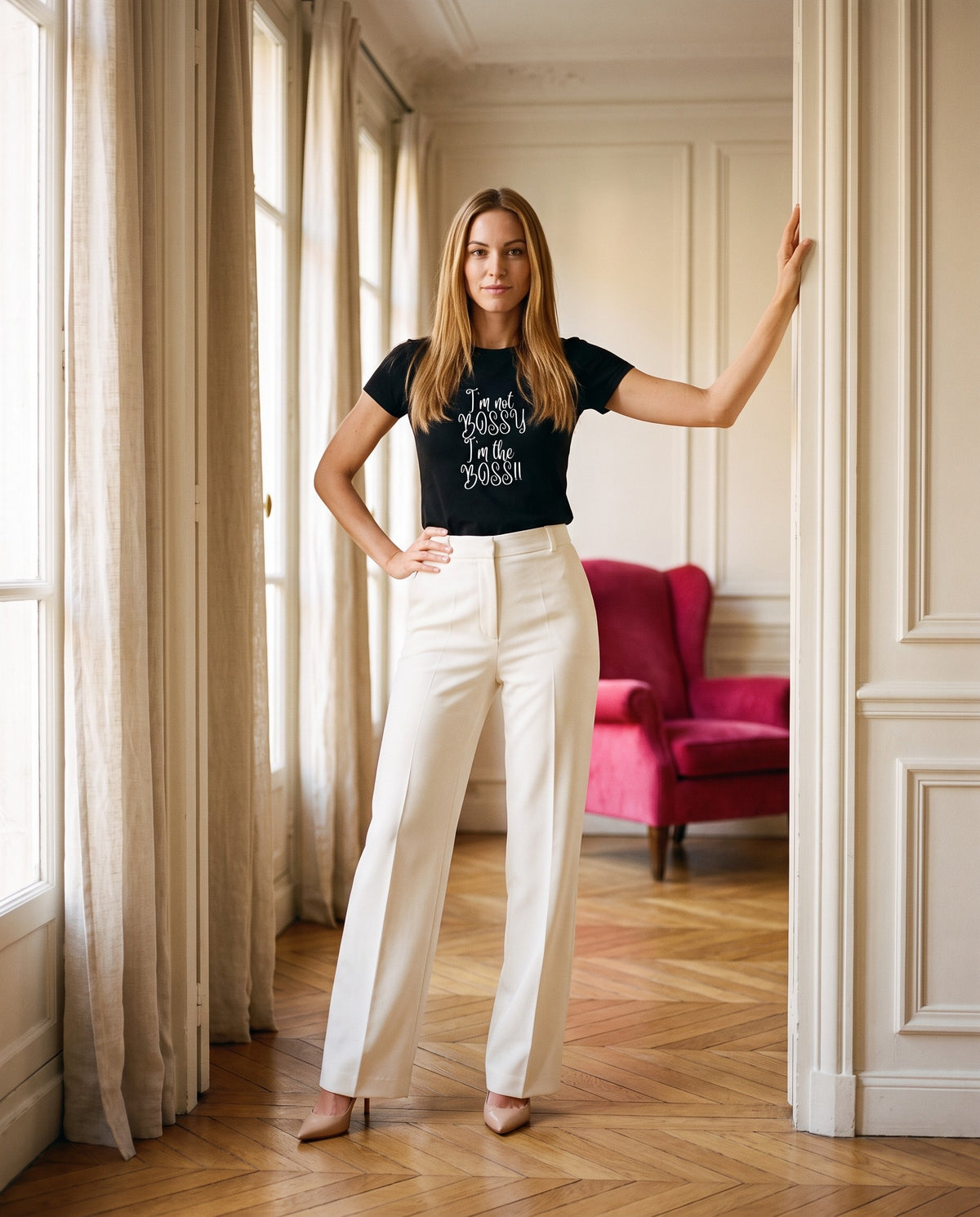 A woman in a black I'm Not Bossy, I'm the Boss tee stands in a doorway, one hand on the frame and one on her hip.
