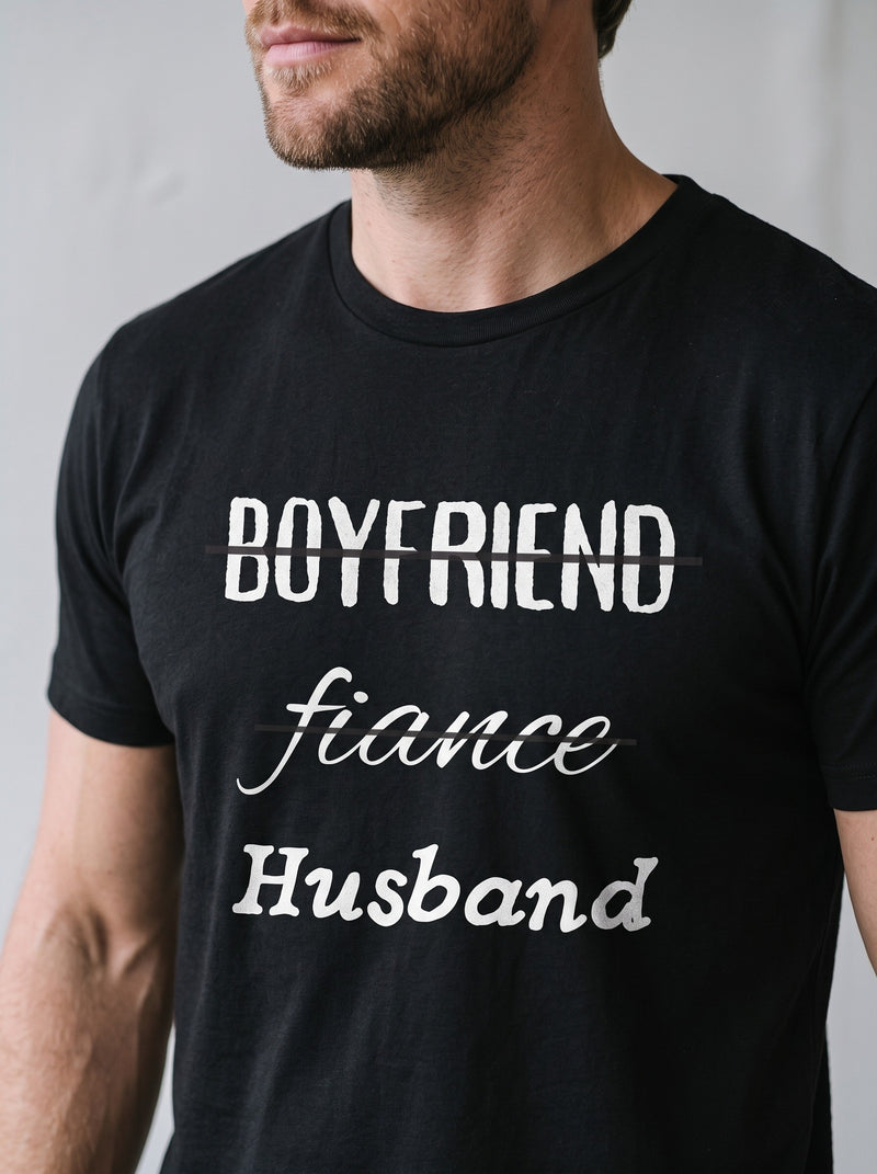 Close-up of a black tee printed Boyfriend, Fiance, Husband, with the first two words crossed out.