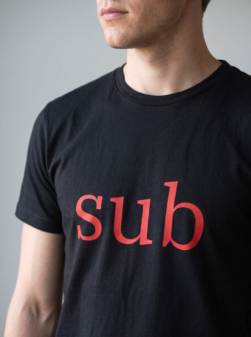 Close-up of a black tee printed with the word sub in red serif letters.
